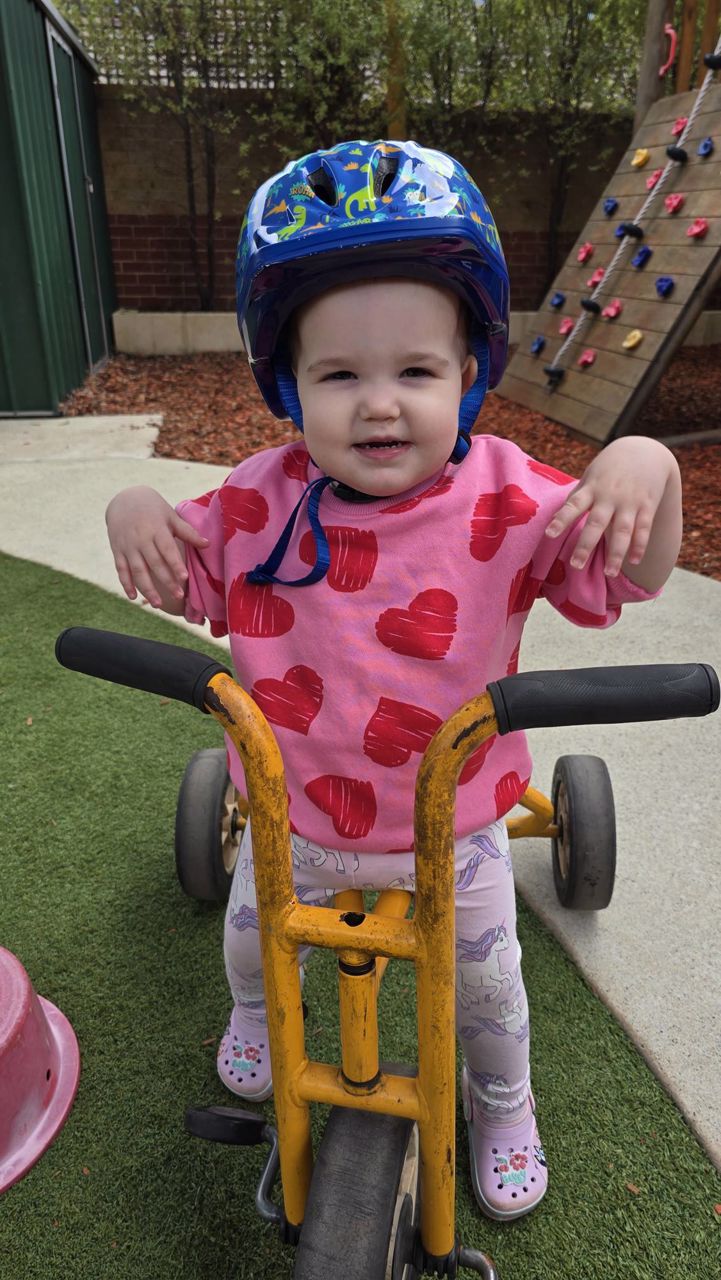 A toddler in a colourful helmet on a tricycle